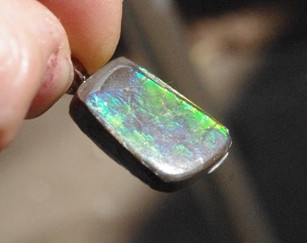 May include: A silver pendant with a green, blue, and iridescent opal stone. The stone is set in a silver bezel and has a rectangular shape.