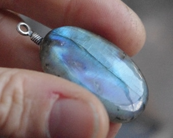 May include: A silver pendant with a blue and green labradorite gemstone. The gemstone is oval shaped and has a smooth, polished finish.