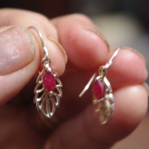 May include: A pair of silver earrings with red gemstone accents. The earrings feature a delicate leaf design.