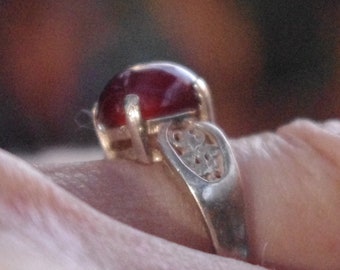 May include: A silver ring with a red gemstone set in a filigree design.