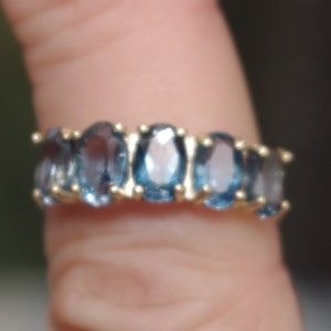 Puede incluir: Un anillo de oro con una fila de piedras azules ovaladas.