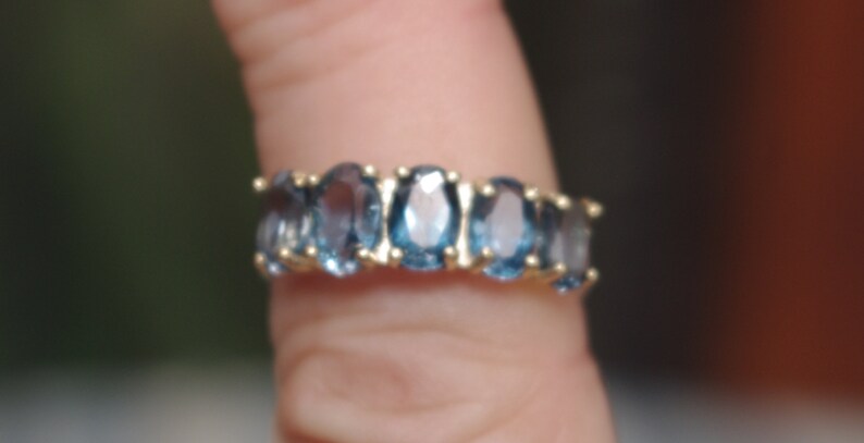 Puede incluir: Un anillo de oro con una fila de piedras azules ovaladas.