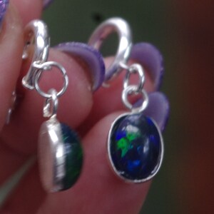May include: A pair of silver earrings with a blue, green and black opal stone pendant. The earrings have a clip-on fastening.