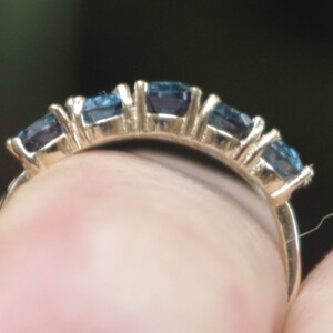Puede incluir: Un anillo de banda de oro con cinco piedras preciosas azules engastadas en fila.