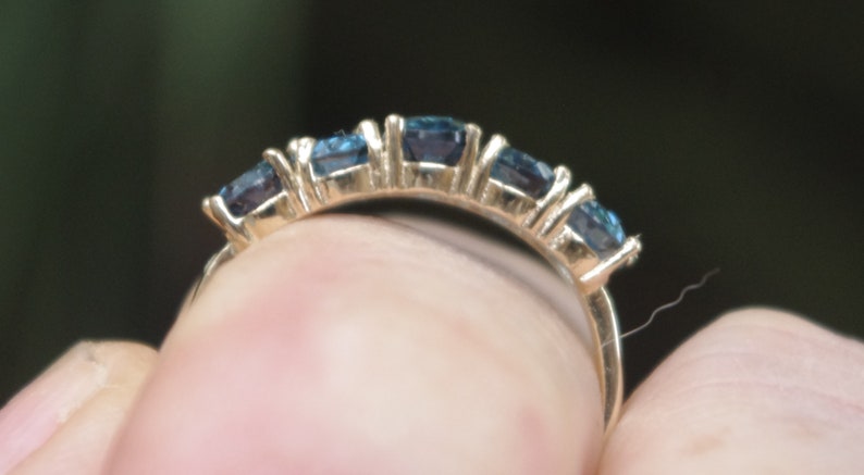Puede incluir: Un anillo de banda de oro con cinco piedras preciosas azules engastadas en fila.