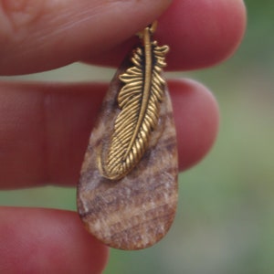 May include: A teardrop-shaped pendant made of wood with a gold-toned feather design.