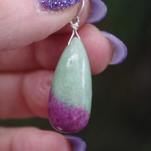 Könnte beinhalten: Ein tropfenförmiger Anhänger aus grünem und rosafarbenem Edelstein mit einer silbernen Öse.