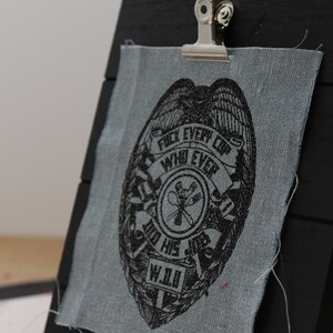 May include: A black and white badge with the text "Fuel Every Cop Who Ever Did His Job W.I.U." printed on a blue fabric patch.