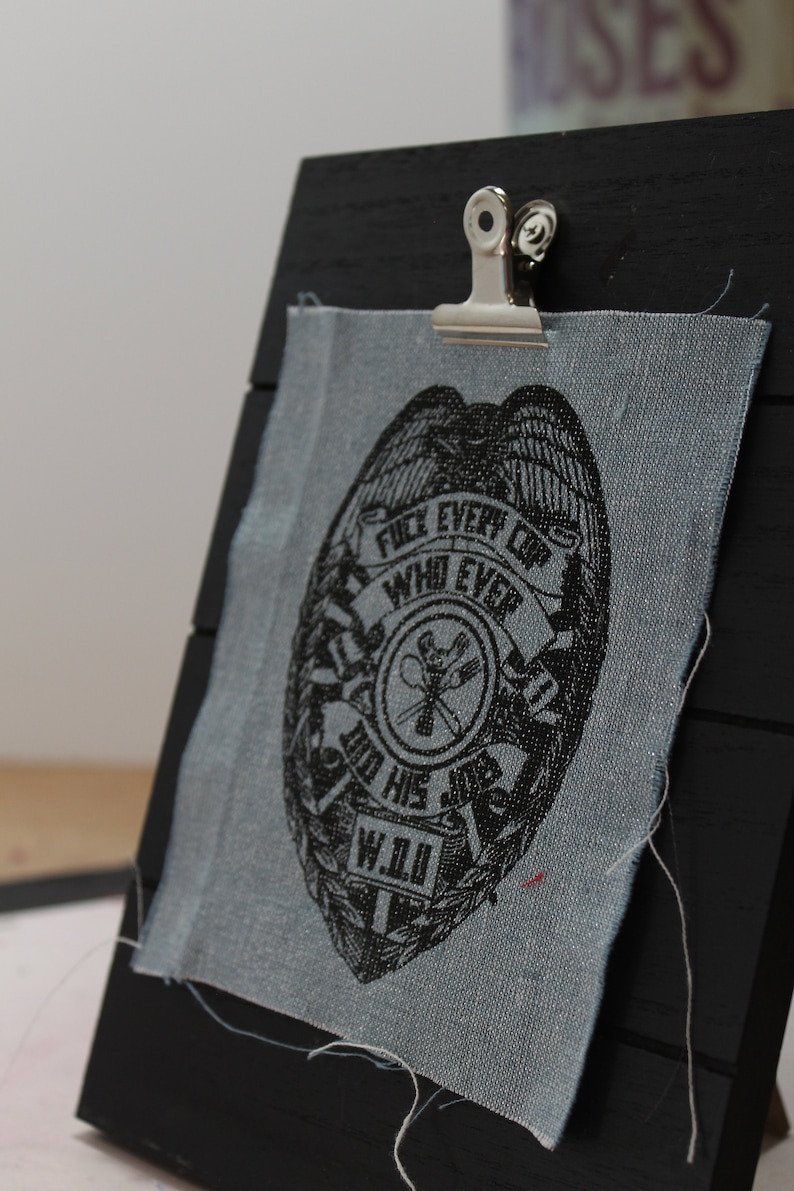 May include: A black and white badge with the text "Fuel Every Cop Who Ever Did His Job W.I.U." printed on a blue fabric patch.
