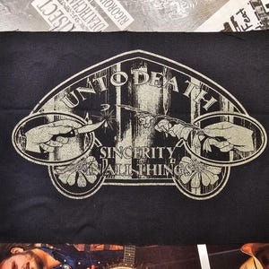 May include: Black patch with a cream-colored design. The design includes the words "UNTO DEATH" in an arch, with "SINCERITY IN ALL THINGS" below. Two hands are depicted, one holding a knife and the other touching a spark.