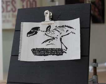 May include: A black and white printed fabric patch with a skeletal creature and the text "I did not think myself frail, until facing the winds of your winter."