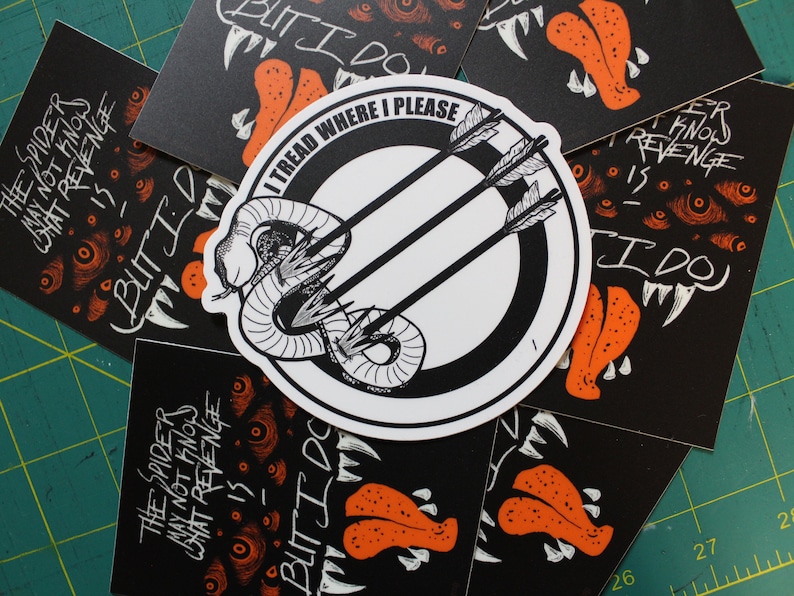 May include: A collection of black and white stickers and cards with illustrations and text. The central sticker features a snake pierced by arrows, with the text "I TREAD WHERE I PLEASE." Other cards have illustrations of a monster and text.