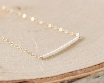 May include: A delicate gold chain necklace with a small bar of white pearls.