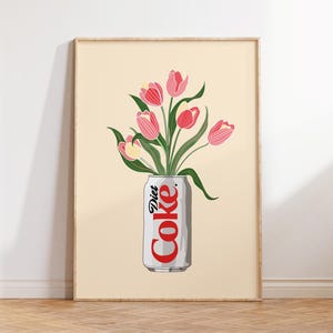 May include: A framed art print showing a Diet Coke can used as a vase for pink tulips. The can is white with red text, and the flowers have green stems and leaves. The background is a pale beige, and the frame is light wood.