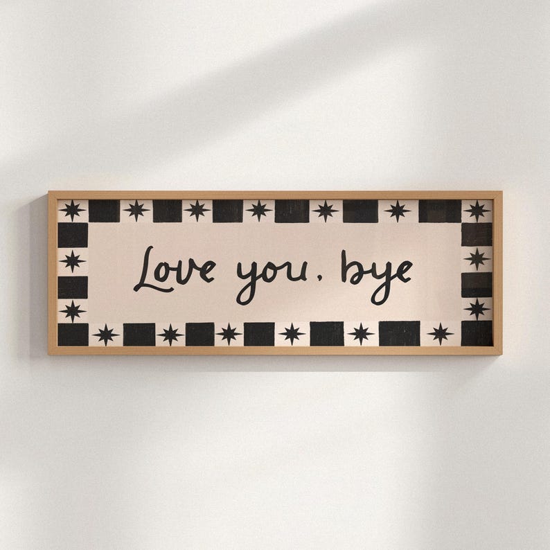 Puede incluir: Cartel rectangular de madera con las palabras "Love you, bye" en escritura negra. El cartel tiene un fondo color crema con un borde de cuadrados negros y estrellas alternas. El marco es de color marr&oacute;n claro.