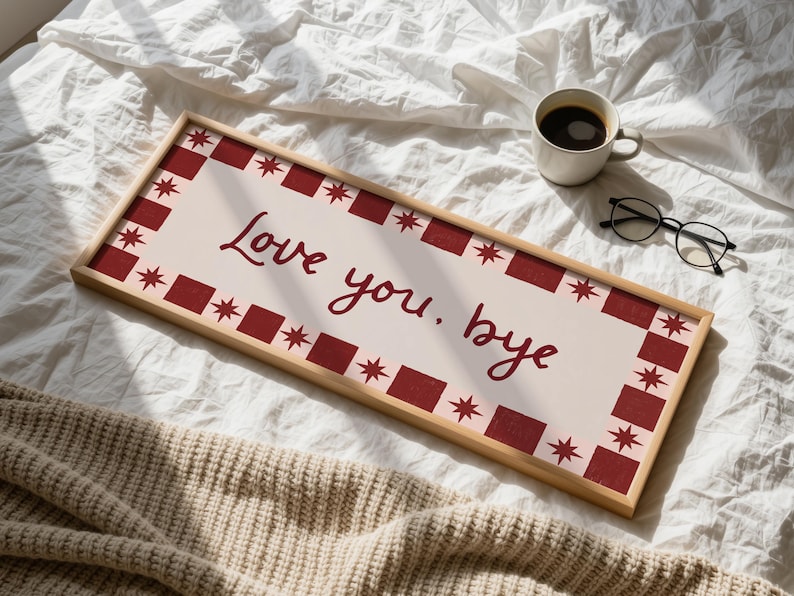 Puede incluir: Un letrero rectangular de madera con las palabras "Love you. bye" en escritura burdeos. El letrero tiene un fondo crema con un borde burdeos de cuadrados y estrellas. Una taza de caf&eacute; y gafas est&aacute;n cerca.