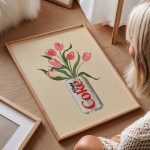 K&ouml;nnte beinhalten: Gerahmter Kunstdruck mit einer Diet Coke-Dose, die mit rosa und roten Tulpen &uuml;berquillt. Die Dose ist geneigt, mit dem Wort "Coke" in Rot. Der Hintergrund ist hellbeige.