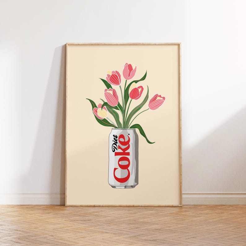 May include: A framed art print showing a Diet Coke can used as a vase for pink tulips. The can is white with red text, and the flowers have green stems and leaves. The background is a pale beige, and the frame is light wood.