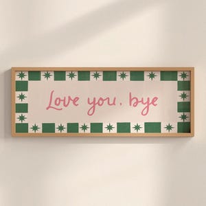 Puede incluir: Un letrero rectangular con marco de madera con las palabras "Love you. bye" en escritura rosa. El letrero tiene un fondo blanco con un borde verde y estrellado.