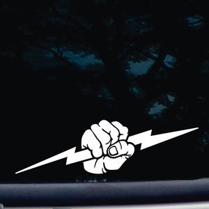 Puede incluir: Calcomanía de vinilo blanco de un puño sosteniendo un rayo. La calcomanía está sobre un fondo negro.