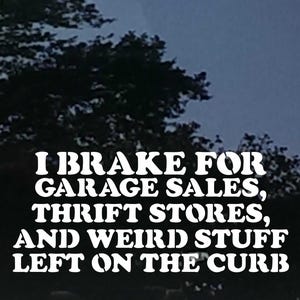 Könnte beinhalten: Weißer Vinyl-Aufkleber mit dem Text "I BRAKE FOR GARAGE SALES, THRIFT STORES, AND WEIRD STUFF LEFT ON THE CURB." Der Aufkleber befindet sich auf einer Autoscheibe, mit verschwommenen Bäumen im Hintergrund.