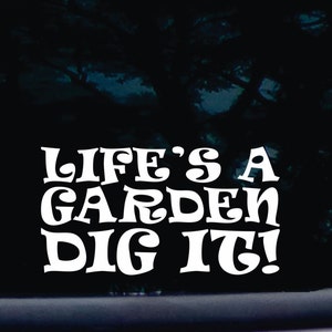 以下が含まれることがあります： レトロなフォントスタイルで「Life's a Garden Dig It!」というテキストが書かれた白いビニールステッカーです。