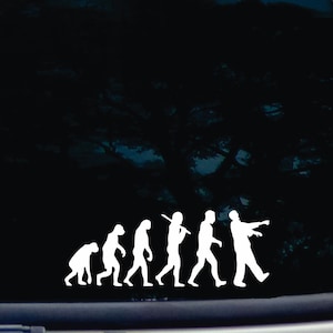 May include: White vinyl decal depicting the evolution of man, culminating in a zombie. The design shows a progression from ape to human, then to a zombie with outstretched arms. Ideal for car windows or laptops.