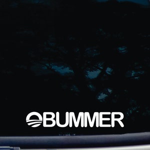 Peut inclure: Un autocollant en vinyle blanc avec le texte "OBUMMER" dans une police de caractères épaisse sans empattement. Le "O" est remplacé par une image stylisée du logo du Parti démocrate, un cercle avec une bande bleue et blanche.