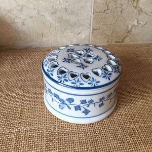 May include: A white ceramic trinket box with a blue and white floral design. The lid has a decorative pattern of hearts and stars with cut-out holes.