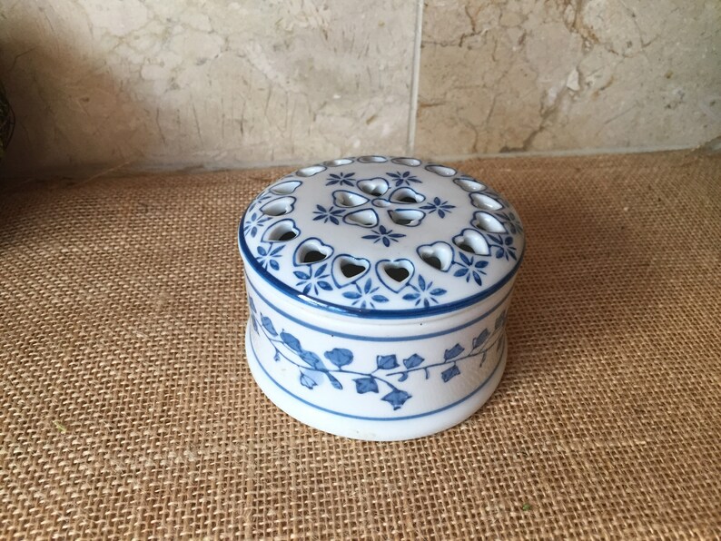 May include: A white ceramic trinket box with a blue and white floral design. The lid has a decorative pattern of hearts and stars with cut-out holes.