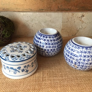 May include: Three ceramic candle holders with a blue and white floral pattern. The candle holders are round and have a small opening at the top for a candle.