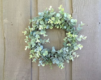 May include: A green eucalyptus wreath with a natural wood base. The wreath is made of artificial eucalyptus leaves and is perfect for adding a touch of greenery to your home decor.
