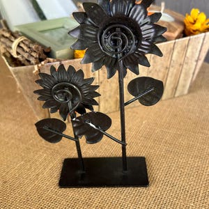 May include: Black metal sunflower sculpture with two flowers and leaves on a black metal base.