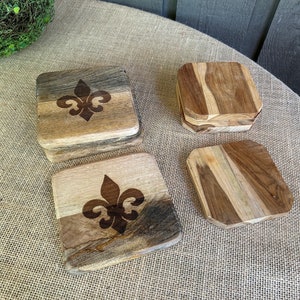 May include: Set of four wooden coasters with a fleur-de-lis design. The coasters are made of different types of wood and have a rustic look.