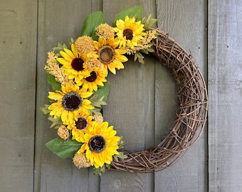 May include: A brown twig wreath decorated with yellow sunflowers and green leaves.
