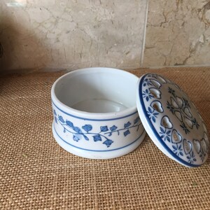 May include: A white ceramic trinket box with a blue and white floral design. The lid has a cutout design and is open.
