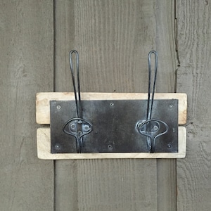 May include: A rustic wooden coat rack with two metal hooks. The rack is mounted on a gray wooden wall.