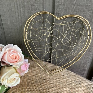May include: A gold heart-shaped wire frame with a delicate, intricate design. The frame is made of thin wire and has a delicate, airy feel.