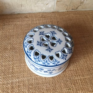 May include: A white ceramic trinket box with a blue and white floral design. The lid has a pattern of hearts and stars with cut-out holes.