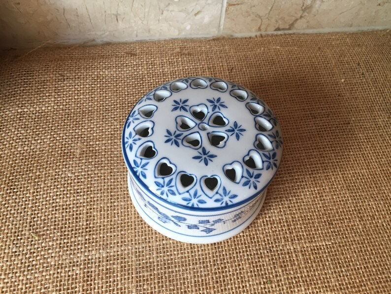 May include: A white ceramic trinket box with a blue and white floral design. The lid has a pattern of hearts and stars with cut-out holes.