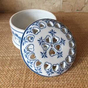 May include: A white ceramic trinket box with a blue and white floral design. The lid has a cutout design of hearts and flowers.
