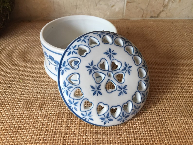 May include: A white ceramic trinket box with a blue and white floral design. The lid has a cutout design of hearts and flowers.