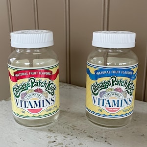 May include: Two clear plastic bottles of Cabbage Patch Kids chewable vitamins with a yellow and green label. Each bottle contains 60 tablets and says "Natural Fruit Flavors".