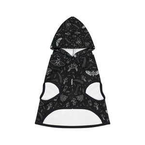 Könnte beinhalten: Schwarzer Hunde-Hoodie mit einem weißen Druck von Motten, Pilzen, Knochen und anderen Waldelementen.
