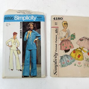 May include: Two vintage Simplicity sewing patterns. One pattern features a woman in a blue pantsuit, the other shows apron designs. The patterns are labeled "Designer Fashion" and "Printed Pattern".