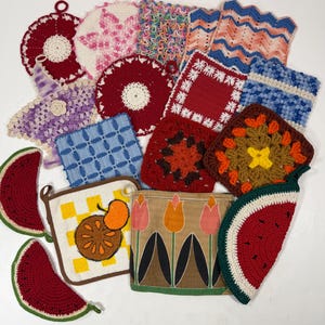 May include: A collection of assorted handmade potholders and kitchen textiles featuring various shapes, colors, and patterns. The items include crocheted watermelon slices, floral motifs, geometric squares, and a fabric square with a tulip print design.