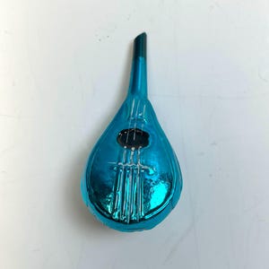 May include: A teal-colored, teardrop-shaped ornament resembling a mandolin. The ornament has a dark green neck and a black sound hole. White lines suggest strings, adding detail to the festive decoration.