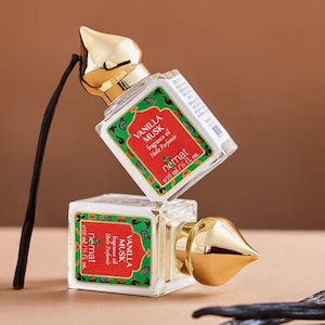 May include: Two small, clear glass bottles of Vanilla Musk fragrance oil with gold-colored caps. Each bottle has a red and green label with the text "VANILLA MUSK fragrance oil" and "nemat e10 ml / 1/3 fl. oz.". A black vanilla bean is next to the bottles.