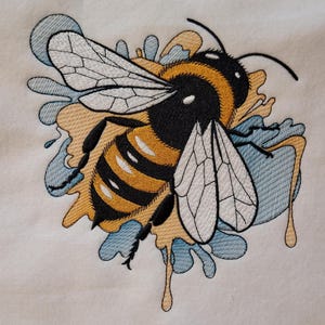 May include: Embroidered design of a bee with yellow and black stripes, surrounded by blue and yellow paint splatters.