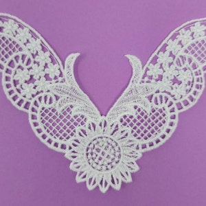 May include: White lace trim with a delicate floral pattern and a scalloped edge. The trim is shaped like a V and is perfect for adding a touch of elegance to any garment.